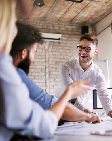 Eine Gruppe von fünf Personen in einem Besprechungsraum diskutiert und arbeitet an Dokumenten. Ein Mann präsentiert aktiv, während die anderen aufmerksam zuhören und Notizen machen.