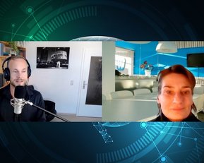Zwei Personen in einem Videoanruf, eine sitzt vor einem Mikrofon mit Kopfhörern, die andere lächelt. Im Hintergrund sind Bücherregale und ein moderner Besprechungsraum sichtbar.