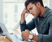 Ein junger Mann sitzt an einem Schreibtisch und schaut konzentriert auf einen Laptop. Er hat eine nachdenkliche Pose eingenommen und hält eine Hand an seinem Kopf.