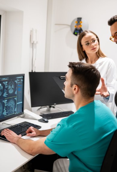 Drei medizinische Fachkräfte besprechen CT-Scans an einem Computerbildschirm in einem modernen Behandlungsraum.