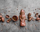 Ein Schokoladenfigur eines Weihnachtsmanns umgeben von Schokoladeneiern und einer kleinen Schüssel mit Schokolade auf einem grauen Untergrund.