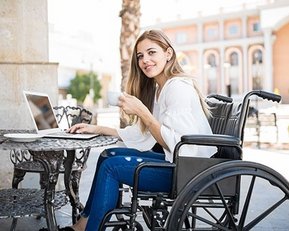 Frau im Rollstuhl mit Notebook an Tisch draußen