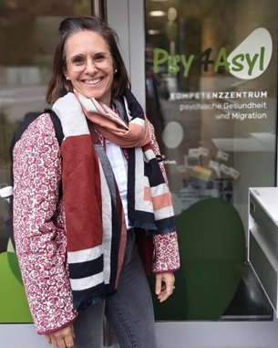 Frau mit Brille und Schal steht vor dem Eingang des Psychiatrie- und Migrationszentrums "Psy 4 Asyl".