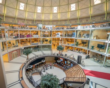 Innenansicht eines modernen, mehrstöckigen Gebäudes mit runden Balkonen, Pflanzen und Sitzbereichen im Zentrum.