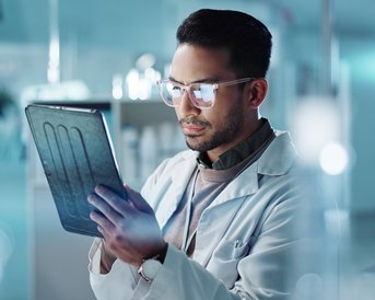 Ein Wissenschaftler in einem Laborkittel betrachtet konzentriert ein Tablet, während er in einem modernen Labor arbeitet.