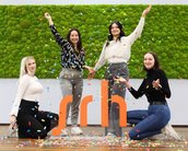 Vier Frauen stehen in einer festlichen Pose, umgeben von Konfetti, vor einer grünen Mooswand. Sie halten sich an den Händen und posieren um das orangefarbene Logo "srh".