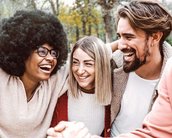 Vier Personen mit unterschiedlichen Frisuren und Kleidung stehen zusammen, lächeln und interagieren. Eine Person hat eine große Afrofrisur, während die anderen längeres, glattes Haar haben. Sie scheinen eine freundliche Unterhaltung zu führen.