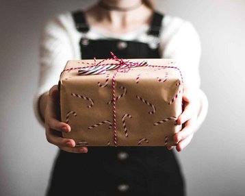 Eine Person hält ein Geschenk in den Händen, das in braunem Papier mit Zuckerstangen-Muster eingewickelt und mit einer roten Schnur gebunden ist.