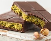 Dunkle Schokolade mit einer Füllung aus grüner Pistaziencreme, die in Stücke geschnitten ist. Im Hintergrund sind einige Pistazienkerne sichtbar.