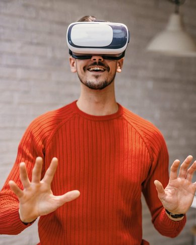 Mann trägt eine Virtual-Reality-Brille und hebt die Hände, als ob er mit einer virtuellen Umgebung interagiert.