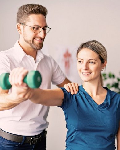 srh-fernhochschule-therapiewissenschaften-ergo Ein Mann hilft einer Frau beim Heben einer Hantel während einer Übungssitzung. Die Frau lächelt, während der Mann sie an der Schulter unterstützt.