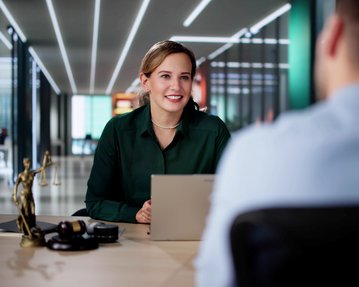 Rechtspsychologie - SRH Fernhochschule Eine Frau in einem grünen Hemd sitzt an einem Tisch und spricht mit einem Mann. Auf dem Tisch steht eine Statue der Justitia.