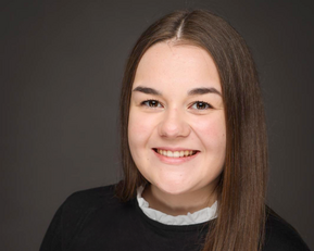 Eine junge Frau mit langen, glatten Haaren und einem freundlichen Lächeln trägt ein schwarzes Oberteil und einen weißen Kragen.