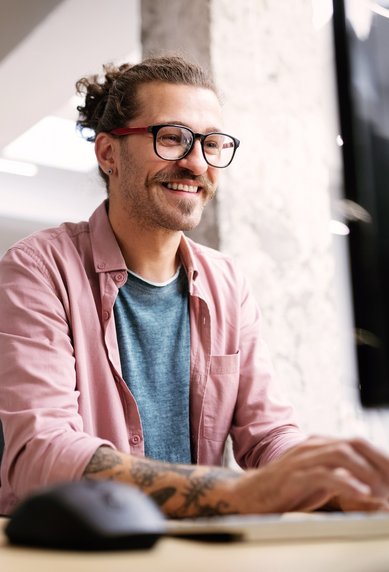 Von der Technik bis zum Content: Ganzheitliche Suchmaschinenoptimierung im Überblick Junger Mann mit Briller und Hemd sitzt vor dem Computer und optimiert eine Webseite
