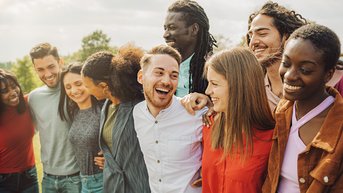 Eine Gruppe von neun Personen steht eng beieinander und lächelt. Sie tragen verschiedene Freizeitkleidung und scheinen eine fröhliche Zeit miteinander zu verbringen. Die Szene vermittelt ein Gefühl von Gemeinschaft und Freundschaft.