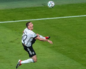 Ein Fußballspieler in einem weißen Trikot mit der Nummer 20 springt, um einen Ball zu erreichen, der hoch über dem Spielfeld fliegt.