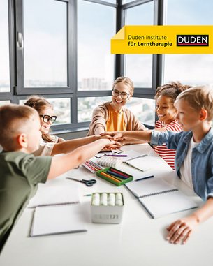 Sechs Kinder und eine Lehrerin sitzen an einem Tisch und legen ihre Hände zusammen. Auf dem Tisch liegen Schreibmaterialien und Notizblöcke.