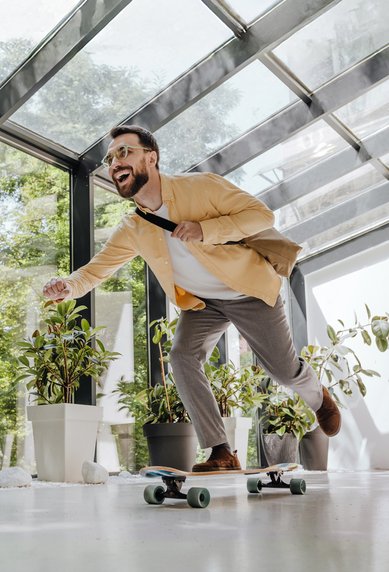 Mann in Anzug fährt auf einem Skateboard in einem modernen Raum mit großen Fenstern und Pflanzen.
