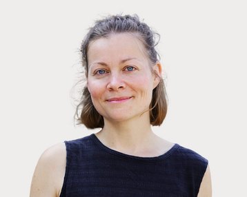 Eine Frau mit kurzen, braunen Haaren und blauen Augen trägt ein schwarzes Oberteil und lächelt freundlich in die Kamera.