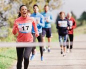 Eine Frau in einem pinken Hoodie und Leggings läuft fröhlich mit der Startnummer 17 auf einem Weg, während mehrere andere Läufer hinter ihr joggen.
